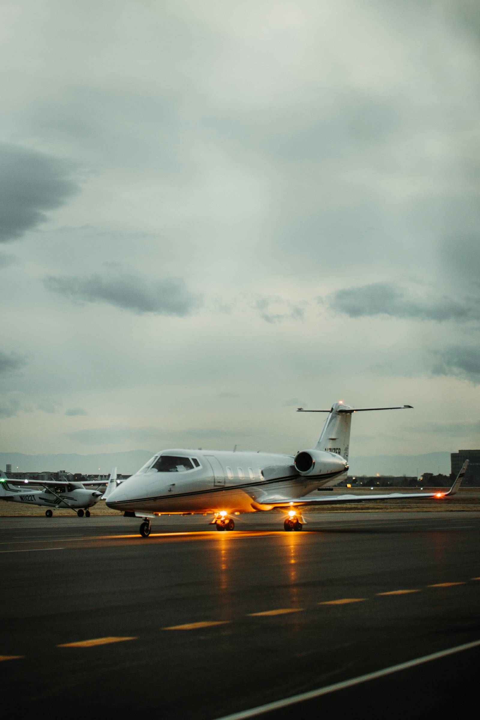 A light business jet taxiing on an airport apron under a pale evening sky