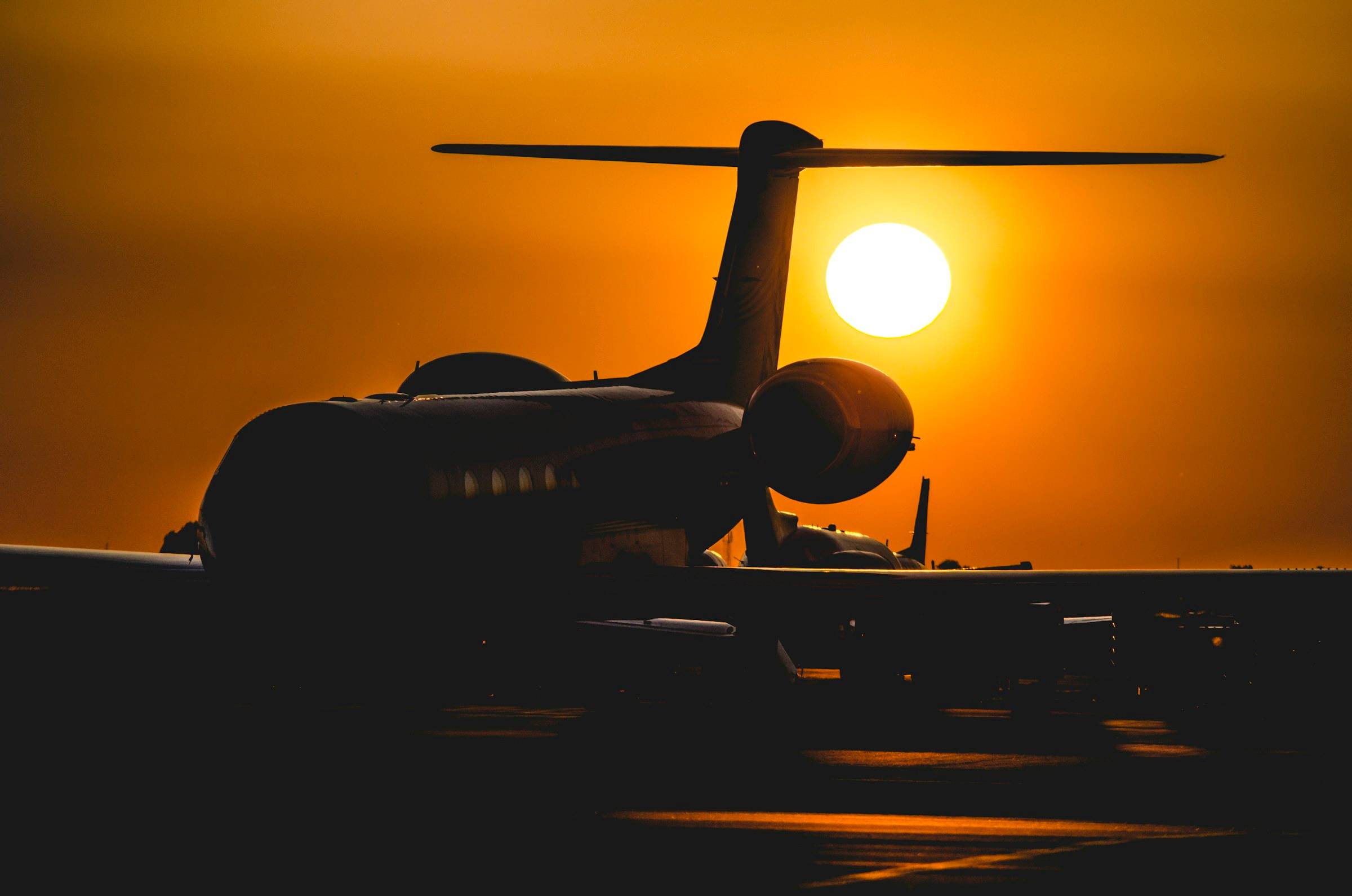 A private jet silhouetted against a low orange sun on the ramp