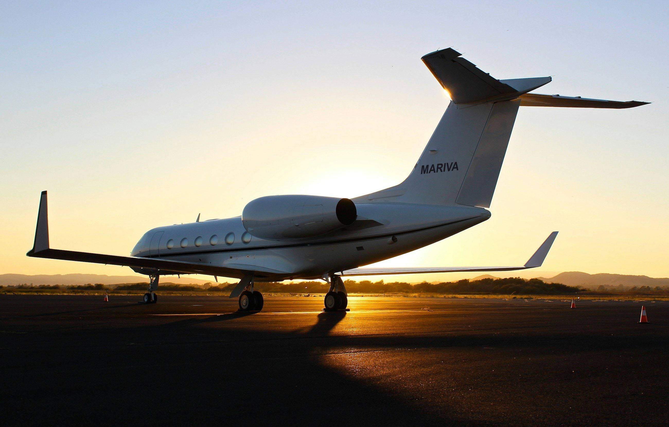 A white business jet on the tarmac at golden hour, sun low behind the tail