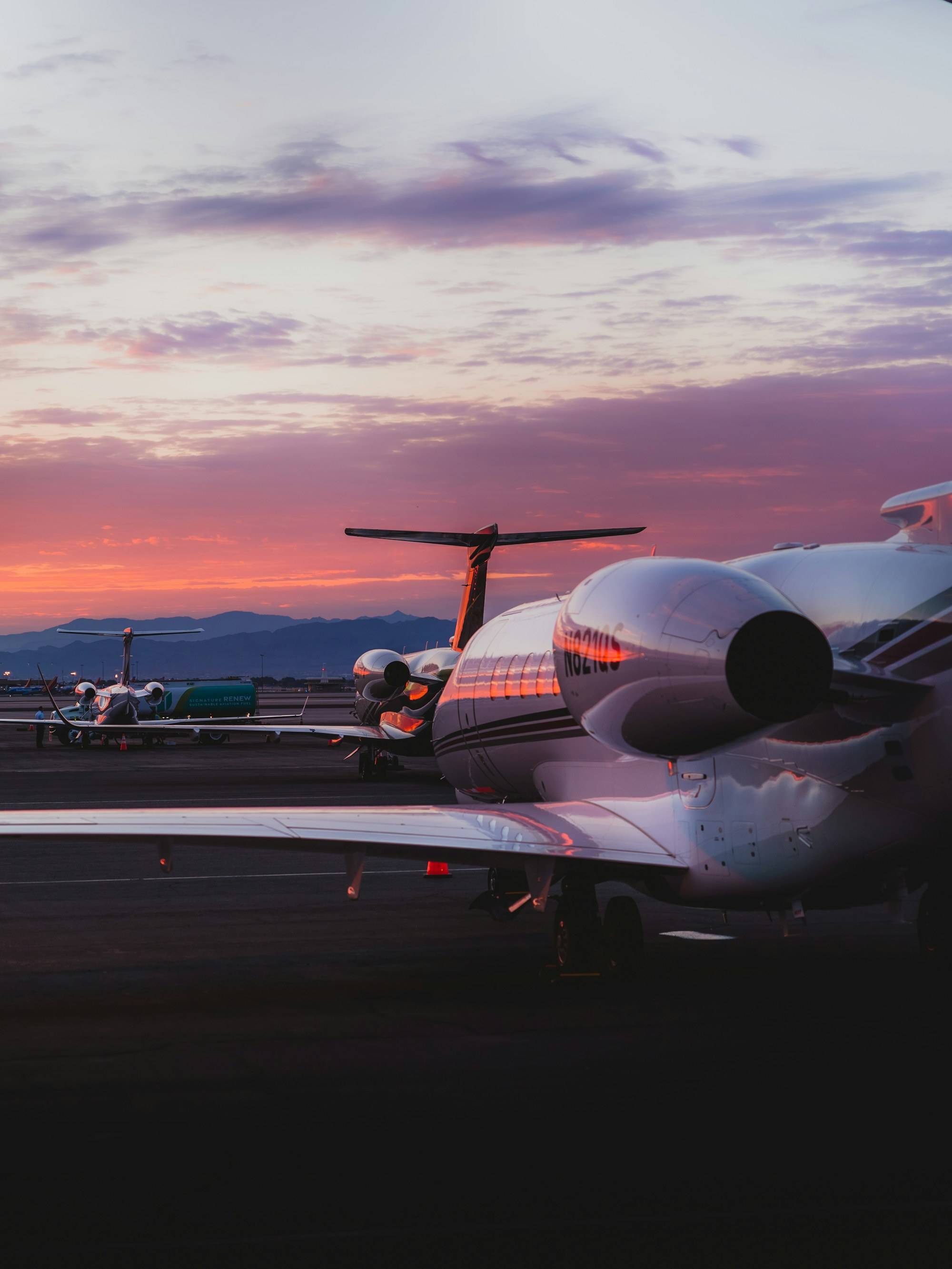 Business jets parked on an airport ramp at dusk with mountains on the horizon